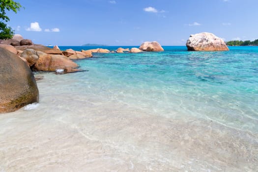 Beach with blue water and blue sky and white sand and some rocks