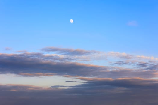 Evening sky with a white moon and lilac-orange clouds