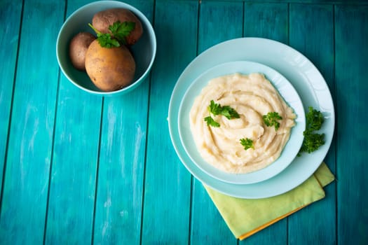 Delicious mashed potatoes with greens in bowl on blue teal wooden table top view