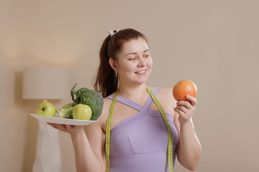 Smiling overweight woman in tracksuit holding healthy fruits and vegetables promoting balanced diet, weight loss and healthy lifestyle.