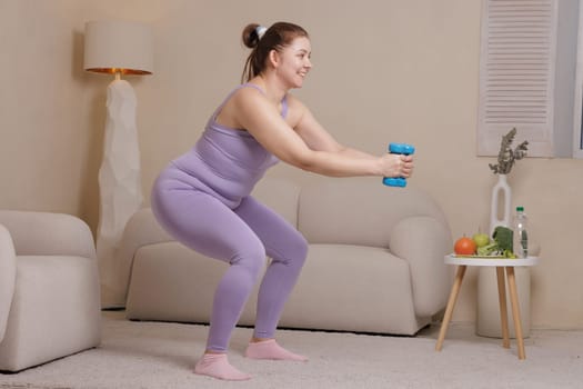 Smiling overweight woman in sportswear doing squats with dumbbells at home promoting fitness, weight loss and healthy lifestyle in cozy interior.