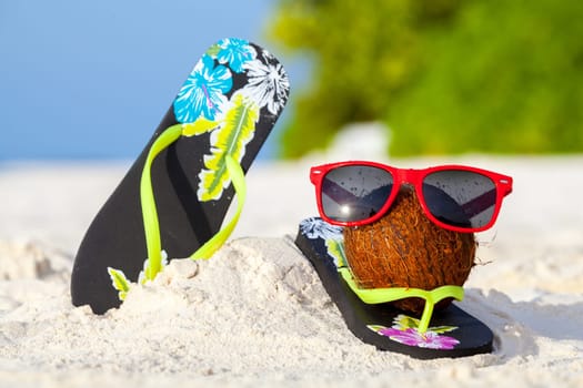 A coconut with sunglasses and shoes on the beach