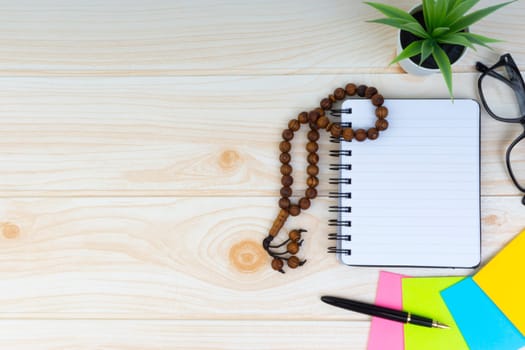 Flat lay view of workspace with Pen, spectacles, decoration flower, rosary and book.Copy Space, business and education concept.