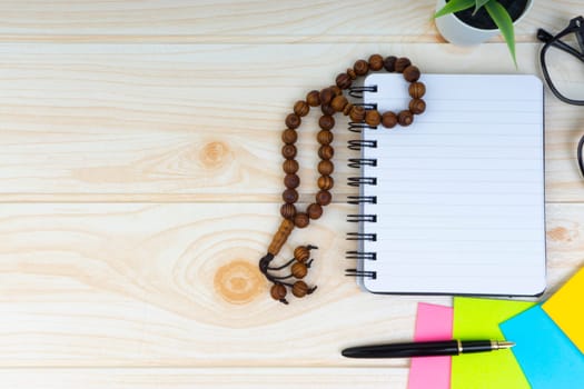 Flat lay view of workspace with Pen, spectacles, decoration flower, rosary and book.Copy Space, business and education concept.