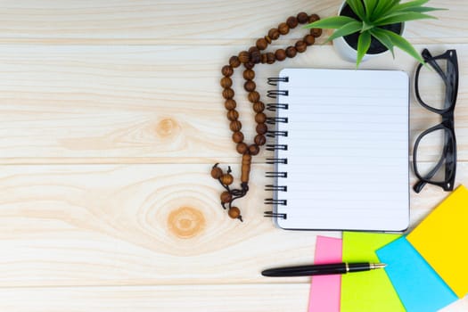Flat lay view of workspace with Pen, spectacles, decoration flower, rosary and book.Copy Space, business and education concept.