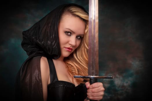 young beautiful woman with a sword in the hand in black cape. Amazon woman.