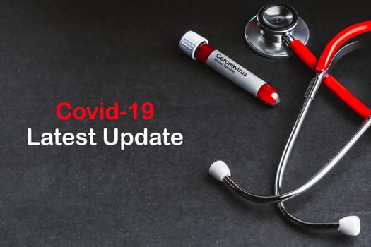 COVID-19 LATEST UPDATE text with stethoscope and blood sample vacuum tube on black background. Covid or Coronavirus Concept