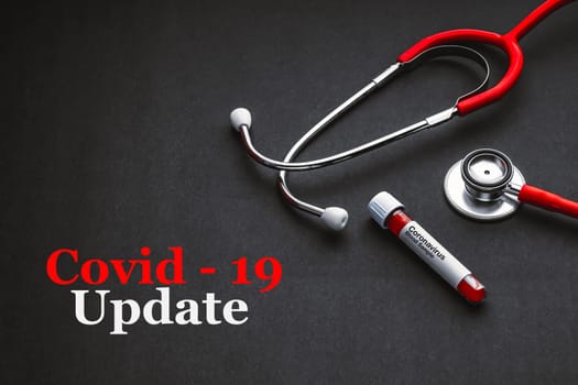 COVID-19 UPDATE text with stethoscope and blood sample vacuum tube on black background. Covid or Coronavirus Concept