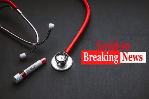 COVID-19 BREAKING NEWS text with stethoscope and blood sample vacuum tube on black background. Covid or Coronavirus Concept