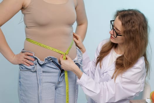 Nutritionist measuring overweight woman's waist with tape in clinic, closeup,