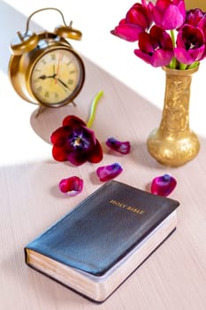 Holy Bible and old gold alarm clock with flowers on wooden table background. Time for studying, reading and spirituality concept.