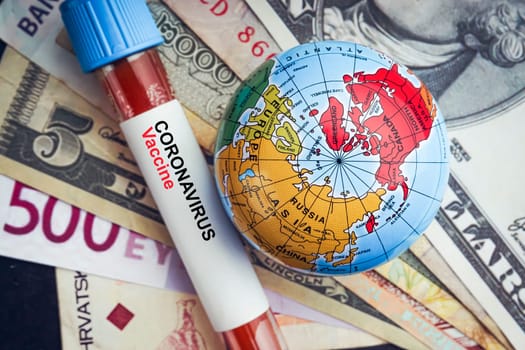 CORONAVIRUS VACCINE text with currency banknotes, world globe and blood test vacuum tube on black background. Covid-19 or Coronavirus Concept