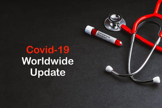 COVID-19 WORLDWIDE UPDATE  text with stethoscope and blood sample vacuum tube on black background. Covid or Coronavirus Concept