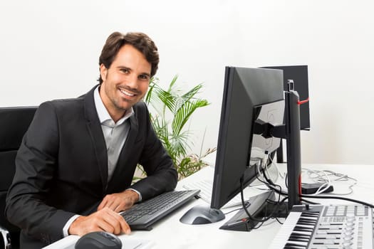 Young successful businessman with black suit in the office at work with computer in concept