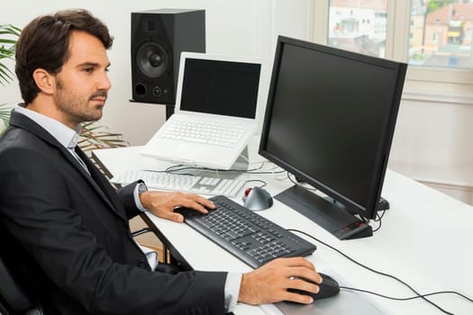 Young successful businessman with black suit in the office at work with computer in concept