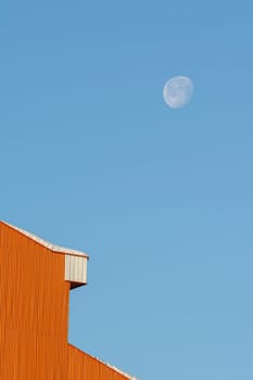 Detail shot of a house building rooftop after a snowfall in winter season, morning moon at blue sky- minimal shot