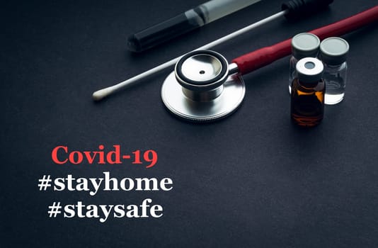 COVID-19 or CORONAVIRUS STAY HOME STAY SAFE text with stethoscope, medical swab and vial on black background. Covid-19 or Coronavirus concept.
