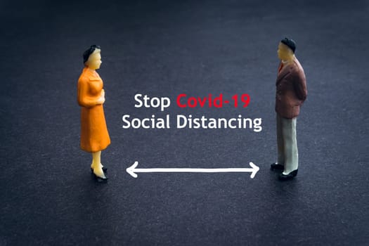 STOP COVID-19 SOCIAL DISTANCING text with miniature people on dark background. Covid-19 or Coronavirus concept
