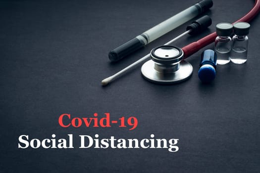 COVID-19 or CORONAVIRUS SOCIAL DISTANCING text with stethoscope, medical swab and vial on black background. Covid-19 or Coronavirus concept.