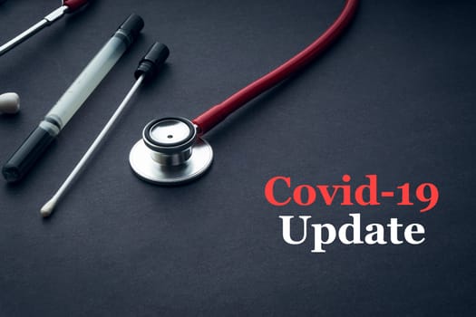 COVID-19 or CORONAVIRUS UPDATE text with stethoscope, medical swab and vial on black background. Covid-19 or Coronavirus concept.