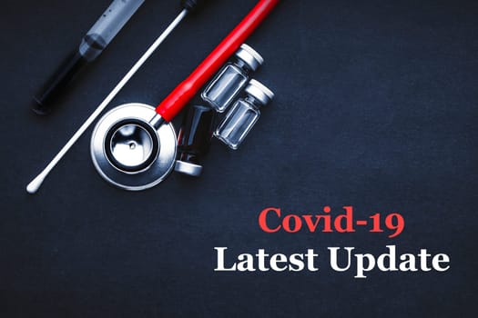 COVID-19 or CORONAVIRUS LATEST UPDATE text with stethoscope, medical swab and vial on black background. Covid-19 or Coronavirus concept.