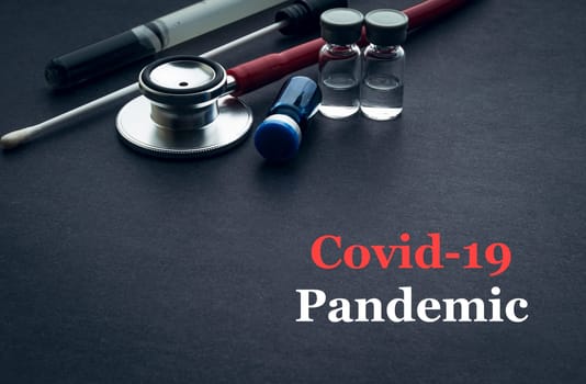 COVID-19 or CORONAVIRUS PANDEMIC text with stethoscope, medical swab and vial on black background. Covid-19 or Coronavirus concept.