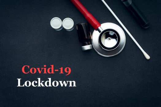 COVID-19 or CORONAVIRUS LOCKDOWN text with stethoscope, medical swab and vial on black background. Covid-19 or Coronavirus concept.