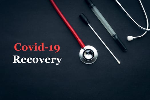 COVID-19 or CORONAVIRUS RECOVERY text with stethoscope and medical swab black background. Covid-19 or Coronavirus concept.