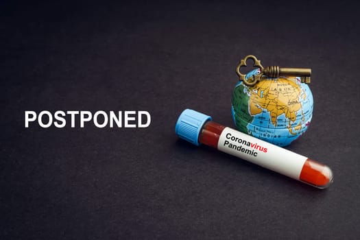 CORONAVIRUS POSTPONED text with world globe, key and Blood test vacuum tube on black background. Covid-19 or Coronavirus Concept