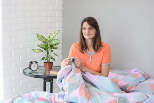 The girl in pajamas woke up and joyfully looks out the window while sitting in bed