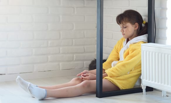 Sad girl sits on the floor under the table, cat sleeps nearby