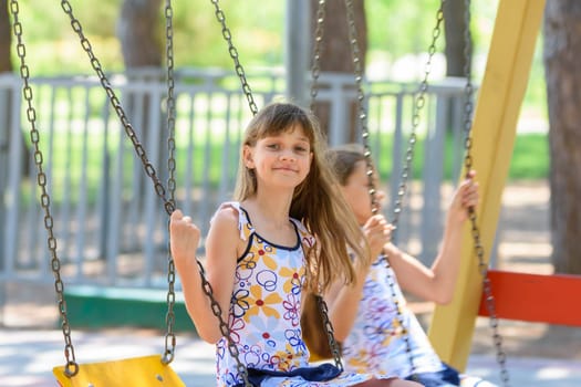 Two girls swing on a swing in a city park