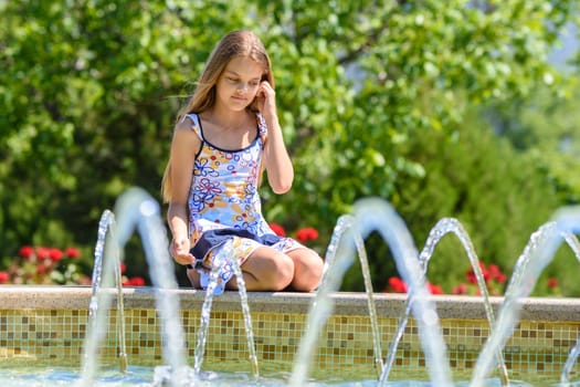 A girl sits at the fountain and looks at the jets of water