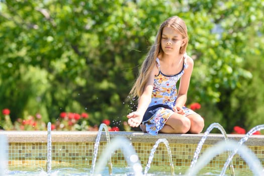 Girl trying to get a jet of water sitting at the fountain in the park
