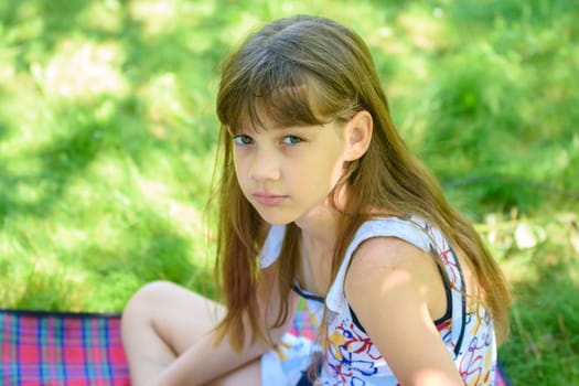 Portrait of a little sad girl on a picnic in a green park
