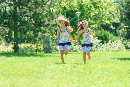 Two little sister run on a green lawn in a park