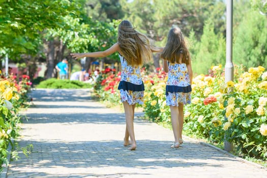 Two little sisters are walking in a beautiful flower city park