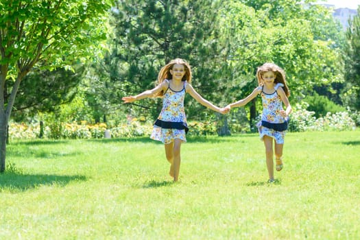 Two girls holding hands run on a green lawn in a park