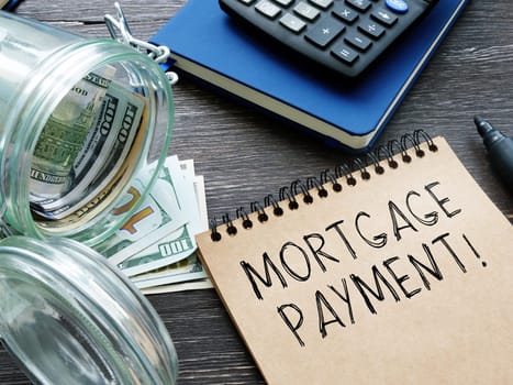 A reminder Mortgage payment written in a notebook. Calculator and jar with money.