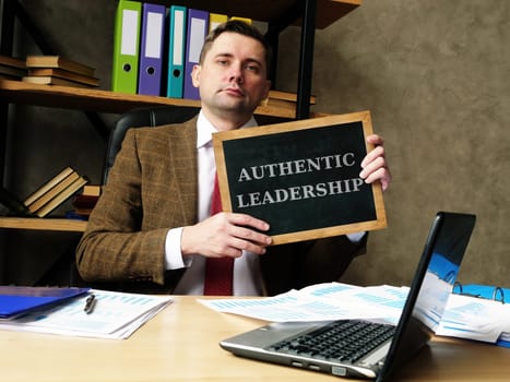 Authentic Leadership concept. Young businessman holds a black board.