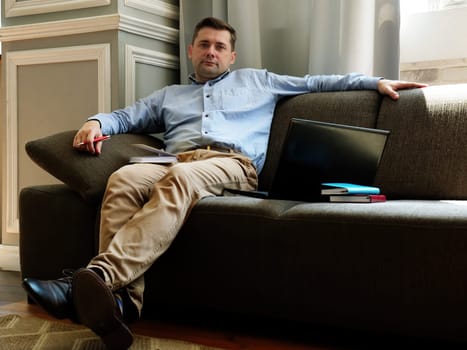 Telework concept. Freelancer is sitting on a sofa with a laptop and papers.