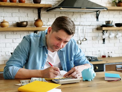 A young man at home calculates the monthly budget. Calculator and piggy bank.