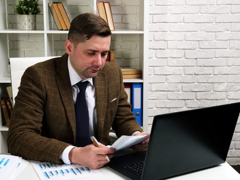 A businessman reads business papers while sitting at an office desk.
