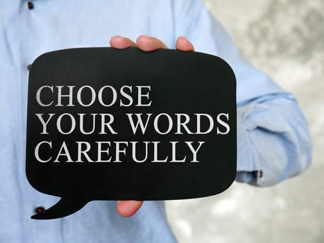 Hand holds a black tablet with the inscription Choose Your Words Carefully.