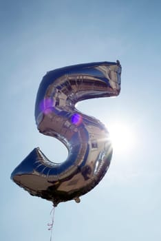 number 5 helium filled balloon against a blue sky