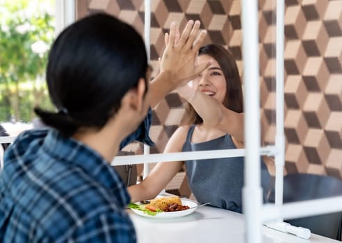 Asian young couple eating out together at new normal social distance restaurant with table shiled partition reduce infection of coronavirus covid-19 pandemic. Restaurant new normal lifestyle.