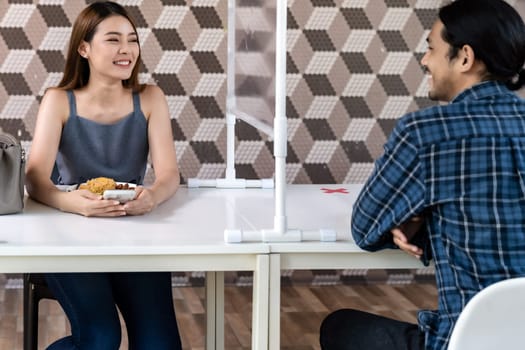 Asian young couple eating out together at new normal social distance restaurant with table shiled partition reduce infection of coronavirus covid-19 pandemic. Restaurant new normal lifestyle.