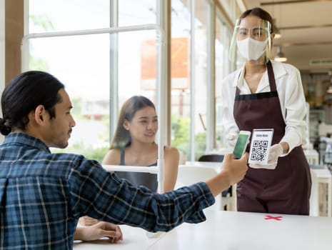 Asian customer scan QR code online menu from waitress with face mask and face shield. Customer sat on social distancing table for new normal lifstyle in restaurant after coronavirus covid-19 pamdemic.