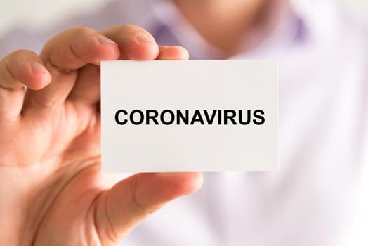 Closeup on businessman holding a card with text Coronavirus, business concept image with soft focus background