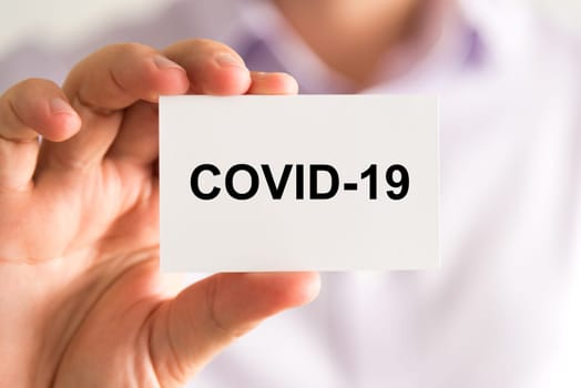 Closeup on businessman holding a card with text Covid-19, business concept image with soft focus background